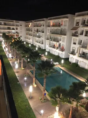 an apartment complex with a pool and palm trees at night at Shems Bouznika Residence Central & Cozy 2 Bedroom Apartment with Pool Bouznika in Bouznika