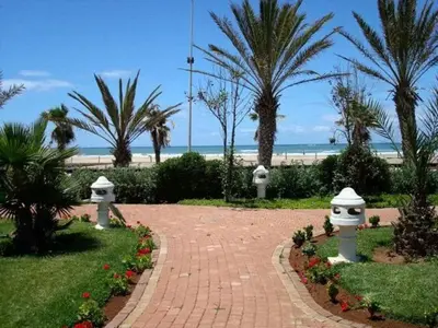 a brick walkway with palm trees and a beach at Appart face à la mer Garden Beach Sidi Rahal plage in Sidi Rahal