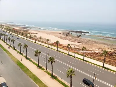 a road next to a beach with palm trees at Apartment with terrace breathtaking ocean views in Rabat