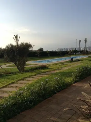 a swimming pool in a park with a tree at Appartement familiale in Tamaris