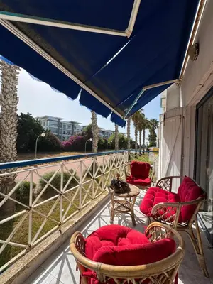 a balcony with chairs and tables and a blue umbrella at Appartement pour la CAN, Palm Beach - Mansouria in Mohammedia