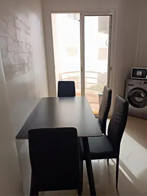a dining room table with chairs and a large window at Kridarek - Bel appartement avec piscine in Sidi Rahal