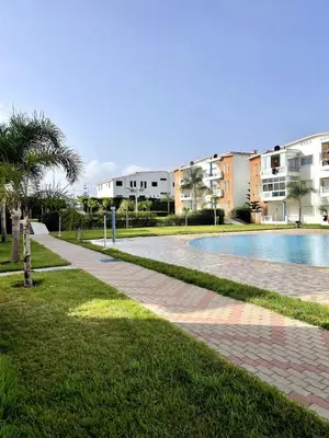 a swimming pool in a park next to a building at Appartement à Sidi Rahal Piscine et Accès direct plage in Sidi Rahal
