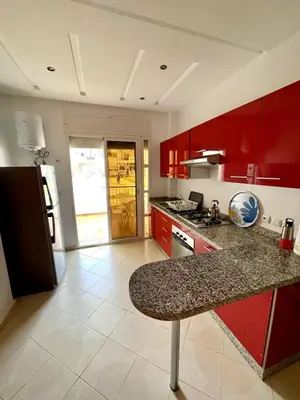 a kitchen with red cabinets and a granite counter top at Appartement à Sidi Rahal Piscine et Accès direct plage in Sidi Rahal