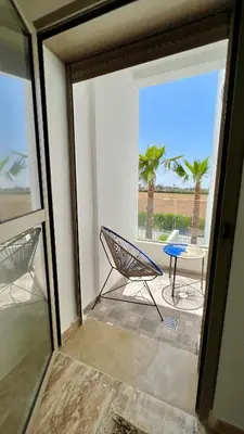 a balcony with a chair and a table and palm trees at Heaven Beach Sidi Rahal in Sidi Rahal