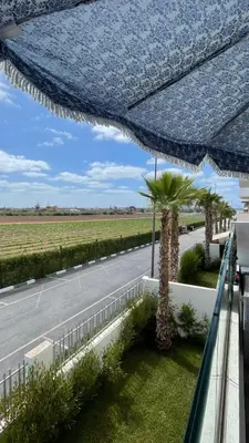 a blue umbrella on a balcony with a road and palm trees at Heaven Beach Sidi Rahal in Sidi Rahal