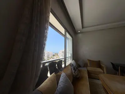 a living room with a couch and a large window at Appartement Residence Mansbay - Piscine - Accès Plage - WIFI in Mohammedia