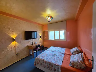 a bedroom with orange walls and a bed and a desk at SUNSET Room in Rabat