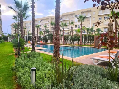 a resort pool with palm trees and a building at Bouznika Apartement de luxe 2 Chambres RDC in Bouznika