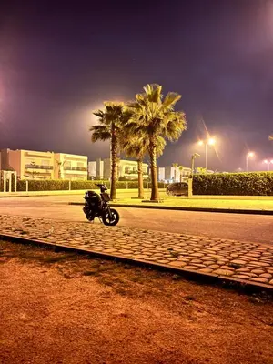 a motorcycle parked on the side of a street with palm trees at Blanca beach in Sidi Rahal