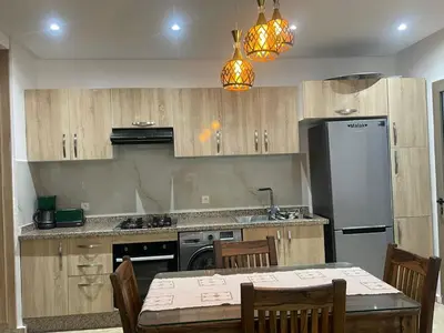 a kitchen with wooden cabinets and a table and a refrigerator at Appartement vu sur piscine à 5 minutes de la plage in Mansouria