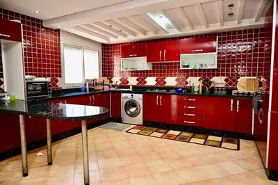 a kitchen with red cabinets and a washing machine at Appartement de Luxe - Piscine et Accès à la Plage in El Harhoura