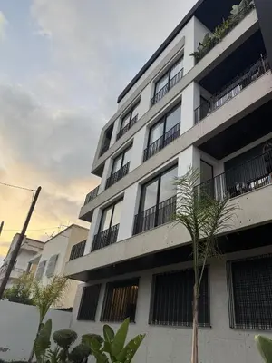 a white apartment building with a palm tree in front of it at Superbe T2 moderne au cœur du Maarif Confort & Style in Casablanca