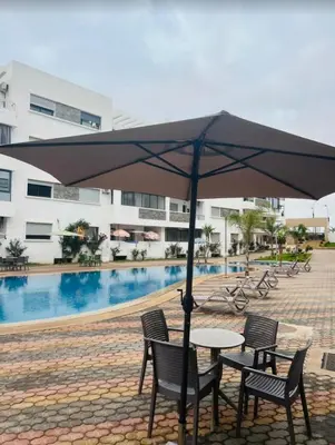 a table and chairs under an umbrella next to a pool at Résidence oasis beach mansouriah in Mohammedia