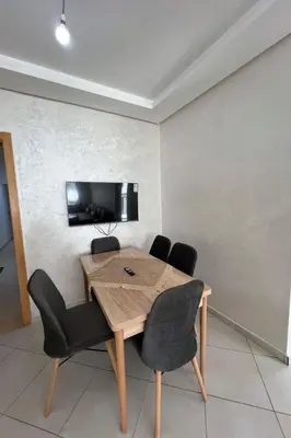 a dining room table with chairs and a television on a wall at Elegant Apartment with Pool & Moroccan Lounge in Bouznika