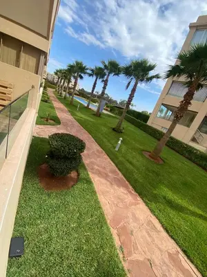 a lawn with palm trees in front of a building at Appartement vue à la mer Bouznika in Sidi el Haj Bou Derbala