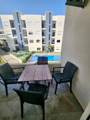 a wooden table and chairs on a balcony with a pool at Apparemment de détente in Mansouria