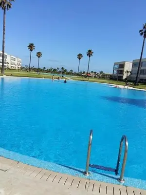 a large blue swimming pool with palm trees in the background at Résidence balnéaire - Piscine Plage et Diverses in Sidi Rahal
