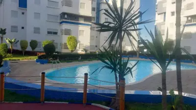 a swimming pool with palm trees in front of a building at La vie de vacances fal azur in Bouznika