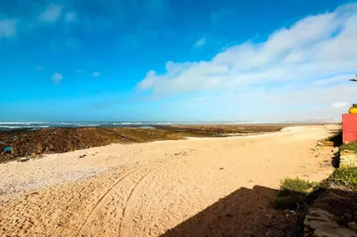 a sandy beach with a red building on it at Casa Nova Maison moderne à deux pas de la plage in Bouznika