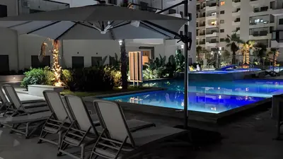 an umbrella and chairs next to a swimming pool at night at VIVASTAY Casablanca - Ocean Park Sunset Escape beach front with swimming pool in Aïn Harrouda
