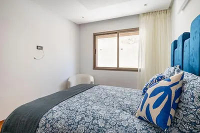 a bedroom with a bed with a blue comforter and a window at Appartement neuf et moderne à l'Agdal, 2 chambres in Rabat