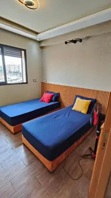 two beds in a room with blue sheets and yellow and red pillows at Bel appartement in Casablanca