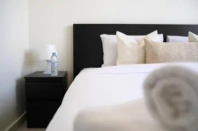 a white bed with a bottle of water on a night stand at Cozy Apartment in the Heart of Bouznika in Bouznika