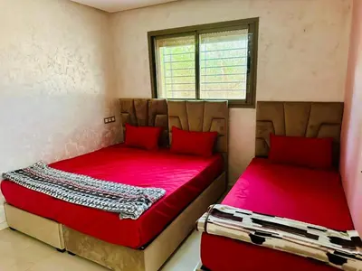two beds in a room with red sheets and a window at Belle maison avec piscine à 7 min de la plage en voiture in Dar Bouazza