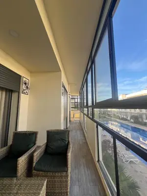a balcony with two chairs and a large window at Elegance Pool View Apartment in Dar Bouazza