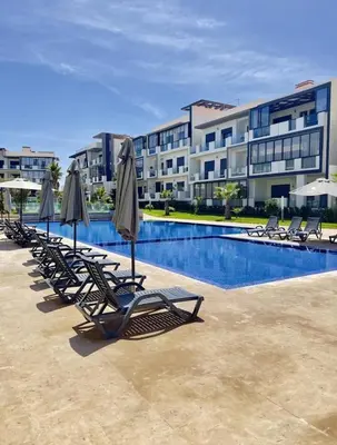 a row of chairs with umbrellas next to a swimming pool at Elegance Pool View Apartment in Dar Bouazza