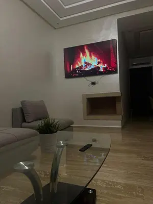 a living room with a fireplace and a tv on the wall at Elegance Pool View Apartment in Dar Bouazza