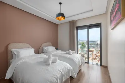 two beds with white sheets in a room with a balcony at Luxury Apartment Perles d'Agdal, Facing Agdal Station in Rabat