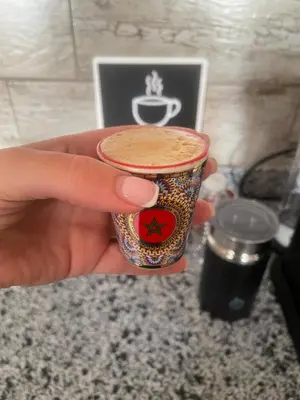 a hand holding a cup of coffee on a counter at Luxury Beach Front Cherrat Plage Apartment in Sidi el Haj Bou Derbala