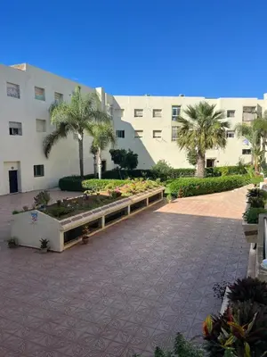 a building with a courtyard with palm trees and plants at Appartement calme et lumineux à Harhoura in El Harhoura