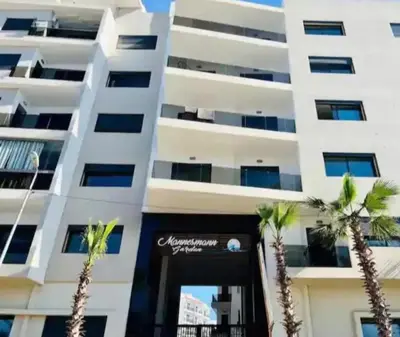 a white building with palm trees in front of it at Apartment in Manesman beach in Mohammedia