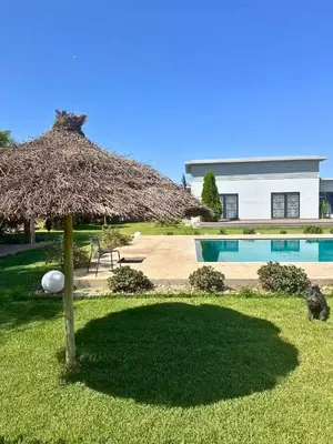 a large straw umbrella in a yard next to a swimming pool at Ferme moderne avec piscine et jardin Sejour paisible au cœur de la nature in Berrechid