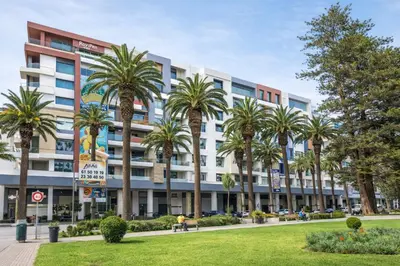 a building with palm trees in front of it at Walkable, Beach in 2, Terrace, DW, AC, PS4, WiFi in Mohammedia