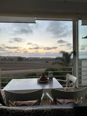 a room with a table and chairs and a large window at Appartement Cosy Bord de Mer in Dar Mohammed Ould Haj Jilali