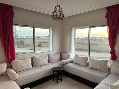a living room with a couch and two windows at Appartement Cosy Bord de Mer in Dar Mohammed Ould Haj Jilali