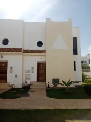 a white building with two doors and a cat in front at Duplex moderne avec jardin privé 5 min de la mer in Skhirat