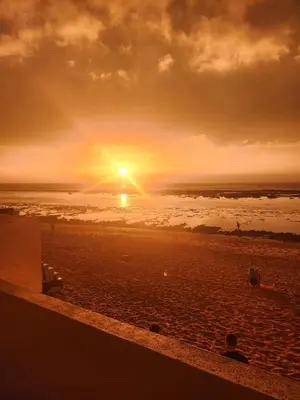 a sunset on a beach with the sun setting at Joumaira beach in Temara