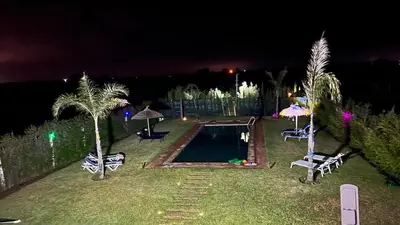 a backyard with a swimming pool and palm trees at night at Ferme royale Bensliman in O Ben Slimane