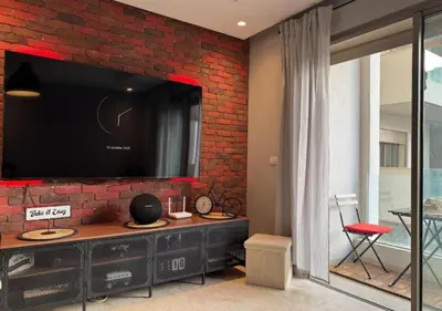 a living room with a large tv on a brick wall at Studio Zenata Central Park Près de la plage Vue Piscine in Aïn Harrouda
