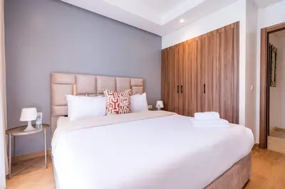 a bedroom with a large white bed and a wooden cabinet at Modern Apartment Pool Balcony & Comfort in Aïn Harrouda