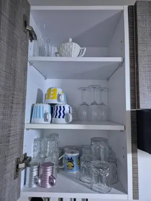 a white pantry with glass items on shelves at Appartement Baraa Havre de sérénité entre mer et nature à tamaris in Tamaris