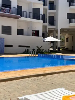 a swimming pool in front of a building with an umbrella at Appartement Moderne avec Piscine in Bouznika