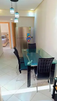 a glass table with chairs and a stainless steel refrigerator at Appartement Moderne avec Piscine in Bouznika