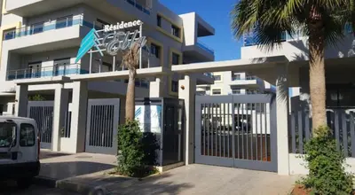 a white building with a gate and a palm tree at Appartement de haut standing à EL MANSOURIA residence EBLA in Pont Blondin