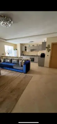 a living room with a blue couch and a kitchen at Appartement de haut standing à EL MANSOURIA residence EBLA in Pont Blondin